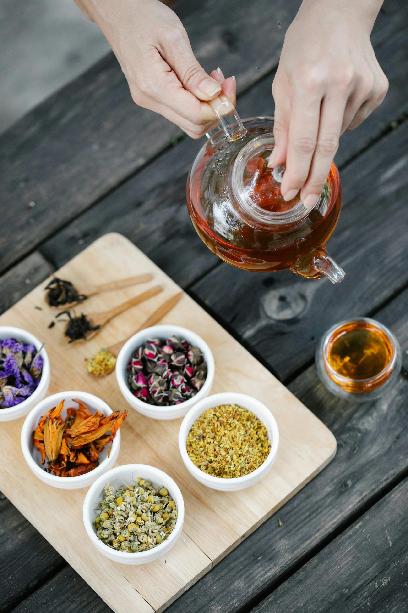Pouring freshly brewed tea beside bowls of botanicals